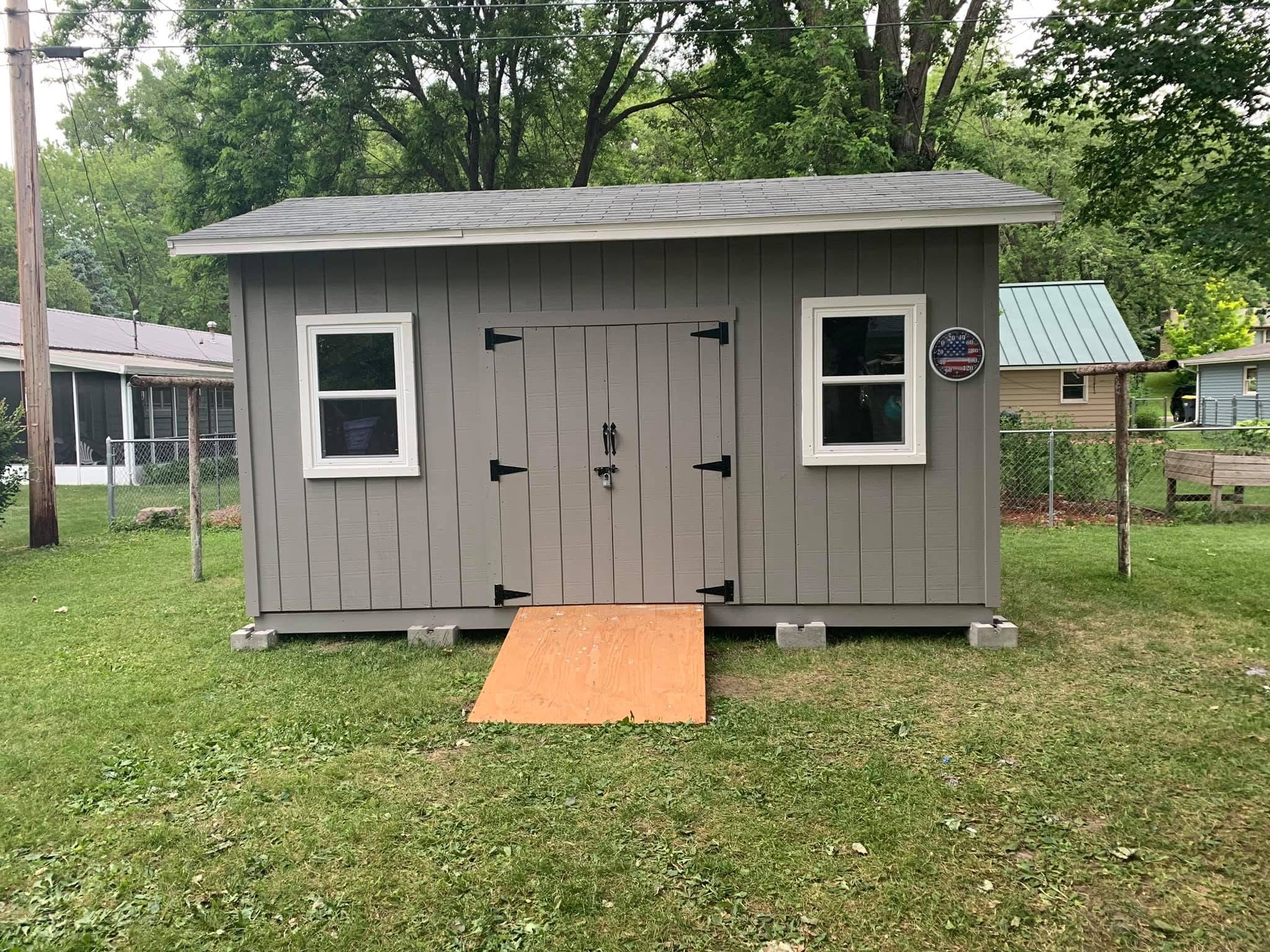 Completed gray backyard storage shed with windows and double doors