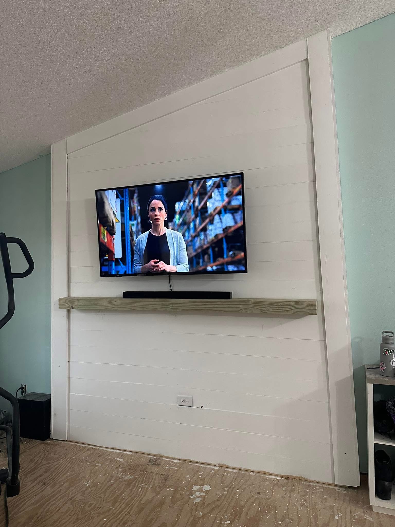 Finished white television feature wall with mounted TV and wood shelf