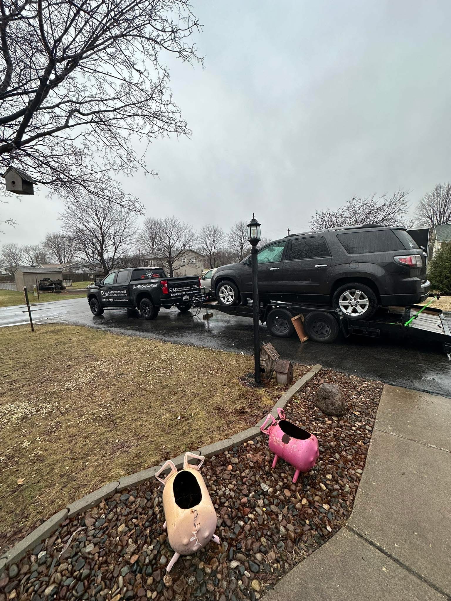 Rustic Memories branded truck towing a black SUV on a flatbed trailer